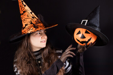 A woman in a witch costume in an orange hat holds a pumpkin lantern jack. People Halloween.