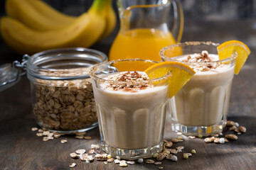 healthy milkshake with oatmeal, banana and orange on dark table, closeup