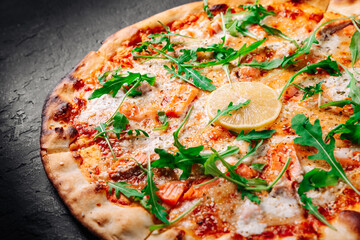 Pizza with Mozzarella cheese, salmon fish, tomato sauce, arugula, lemon. Italian pizza on Dark grey black slate background