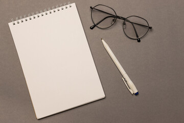 A blank sheet of spiral notebook paper, glasses and a pen on a gray background, top view. Business concept. Distance learning for students and schoolchildren.