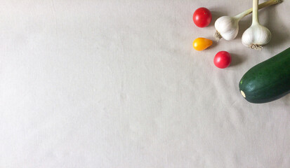 Green zucchini, heads of garlic and cherry tomatoes on beige background. Fresh vegetables contain vitamins and are good for health. Autumn. Space for text, flat lay, minimal concept. Healthy food