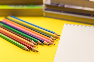 Obraz premium A blank sheet of notepad with colored pencils and books on a yellow background. Knowledge Day. Back to school.