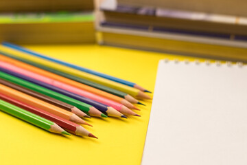 Colored pencils and a blank sheet of drawing paper on a yellow background. Preparation for drawing. A fine art lesson at school.