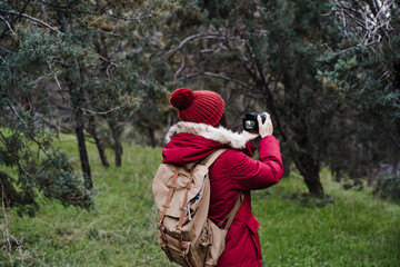 backpacker caucasian woman taking picture with camera in forest during winter or autumn season. Lifestyle and nature