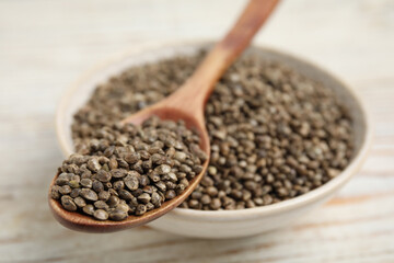 Bowl and spoon with organic hemp seeds on white table, closeup