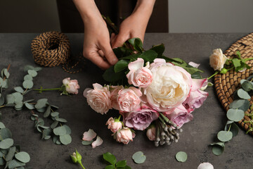 Florist creating beautiful bouquet at black table indoors, closeup