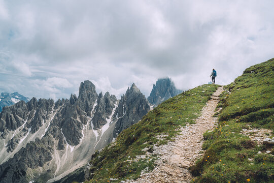Woman trekker with a backpack with trekking poles enjoying picturesque Dolomite Alps view near Tre Cime di Lavaredo formation in South Tyrol, Italy. Active people and mountain concept.