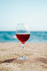  Glass of red wine against the background of the Mediterranean beach and the sea in a tourist town in the summer under sunlight. Summer, travel, lifestyle, relaxation, and enjoyment concept.