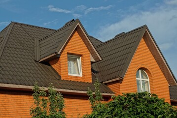 big attic of a private red brick house with windows under a brown tiled roof against a blue sky