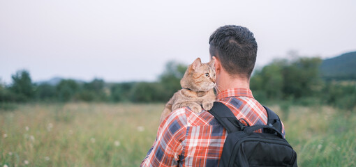 Cat sitting on shoulder of man in summer park.