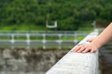 Close-up at people hand during place on concrete barrier wall structure of water reservoir or barrage, with blurred background of nature environment. People loneliness action abstract photo. 