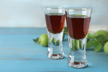 Delicious liqueur and green walnuts on light blue wooden table, closeup. Space for text