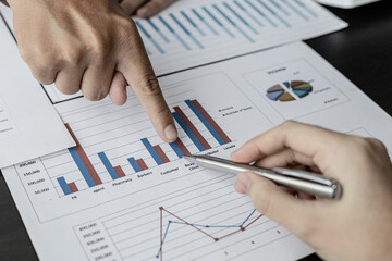 Close-up photo of two businessmen pointing at a sales data sheet in graph format, they are meeting together on the topic of managing sales growth. Concept of business cooperation and sales management.