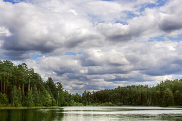 Beautiful cloudy sky over forest lake, summer landscape