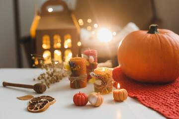Cozy autumn composition with pumpkin, wax candles, dry leaves by bokeh lights background. Fall, Halloween, Happy Thanksgiving concept