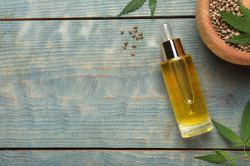 Hemp oil, seeds and leaves on light blue wooden table, flat lay. Space for text