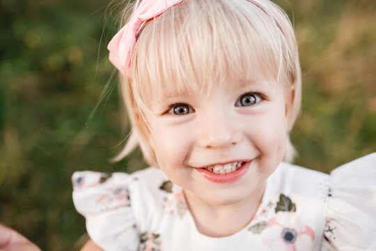 Portrait of a little beautiful girl on nature on summer day vacation. child in dress is playing in the green park at the sunne time. The concept of family holiday and time together