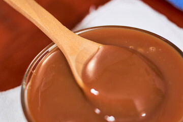 Dulce de leche in glass container, on wooden table, Cajeta. Argentine food concept.
