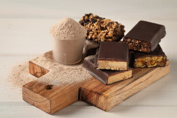 Different tasty energy bars and protein powder on white wooden table
