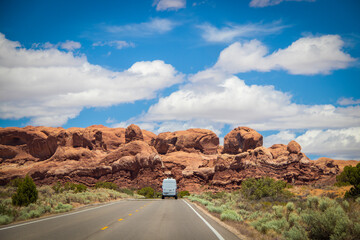 White camper van drives toward red rock formation at Arches National Park in Utah USA.