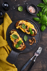 Scrambled eggs with fried mushrooms and basil on bread on black table background. Homemade breakfast or brunch meal - scrambled eggs and mushrooms sandwiches. Top view with copy space