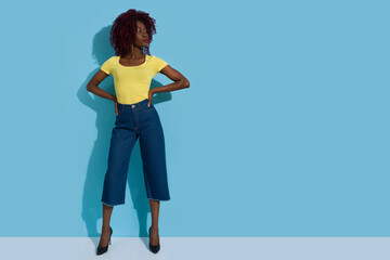 Confident Young Black Woman Is Standing Against Blue Wall And Looking To The Side