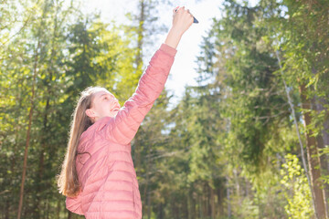 Fototapeta premium Young teen girl traveler taking selfie on mobile phone in a summer day forest. girl looking at smartphone camera.