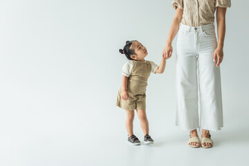 asian toddler kid holding hands with stylish mother on grey