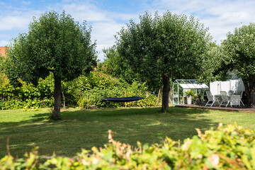 Beautiful garden design. Hammock for rest and relaxation stretched between trees in garden. Well mowed grass on lawn near cottage villa. White wood outdoor furniture. Greenhouse in courtyard of house.