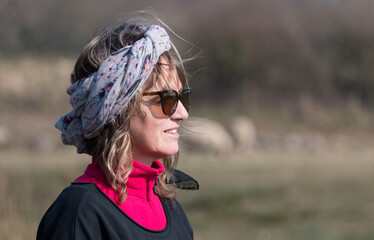 An attractive lady looks right with a headscarf long hair on windy but sunny day wearing...