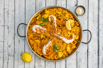 Great mixed seafood and chicken Valencian paella presented in a paella pan with squid, prawns, mussels and chunks of stewed chicken and aioli sauce