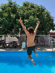 Niño saltando a la piscina en verano con mascota mirando al fondo