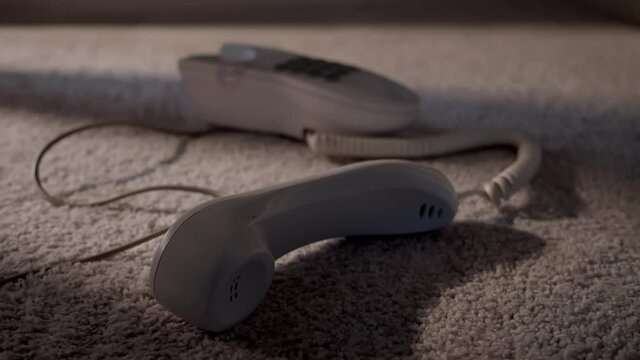 1980s or 90s style corded home telephone on the floor with the phone off the hook with mysterious shadow walking away.