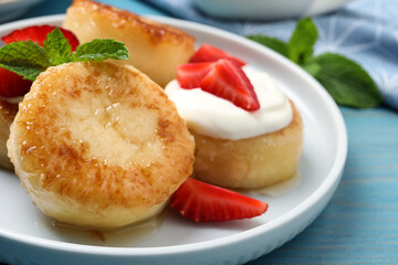 Delicious cottage cheese pancakes with strawberries, honey and sour cream on light blue wooden table, closeup
