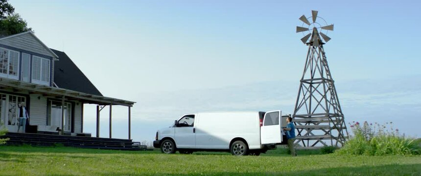 WIDE HANDHELD Hispanic male delivering package, bringing box from van to a house. White van with copy space. Shot with 2x anamorphic lens