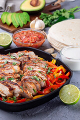 Grilled chicken Fajitas with bell pepper and onion in a pan, served with salsa Asada, sour cream, avocado and tortillas, vertical