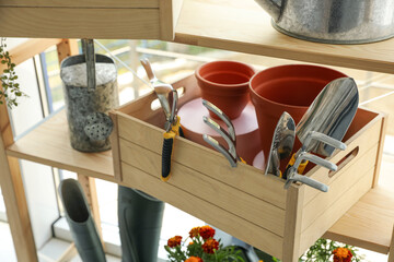 Wooden crate with gardening tools on rack indoors