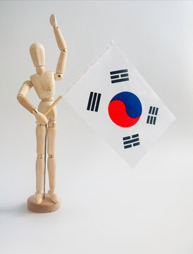 Wooden mannequin, doll, dummy, puppet, figure of little person, waving or holding the flag of South Korea, isolated on white background, text space. Supporter, celebration and national pride concept.
