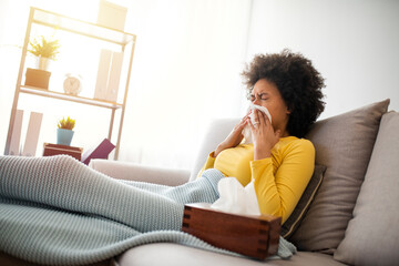 Sick Woman Covered With a Blanket Lying in Bed With High Fever and a Flu, Resting at Living Room. She Is Exhausted and Suffering From Flu. Sick Woman With Runny Nose Lying in Bed