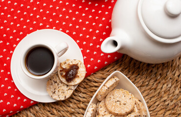 A cup of coffee under the straw table surrounded by a bowl full of rice cookies and a coffee pot
