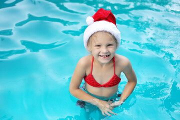 a little happy girl in a Santa Claus hat and a red swimsuit in the pool