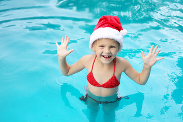 a little happy girl in a Santa Claus hat and a red swimsuit in the pool