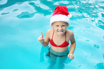 a little happy girl in a Santa Claus hat and a red swimsuit in the pool