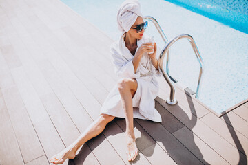 Young woman in bathrobe drinking coffee by the pool