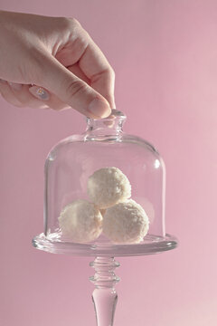 round sweet candies in coconut shavings in a glass vase on a pink background, harmony of taste, exquisite dessert, hand takes rafaello