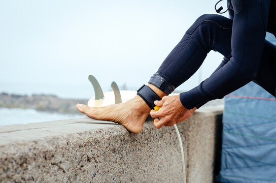 Closeup of young man putting on surfboard leash on beach. Guy wearing wetsuit and standing
