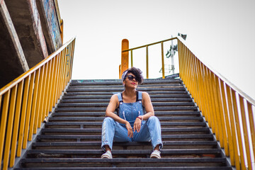 Mid adult afro mexican woman sitting on some urban steps relaxing