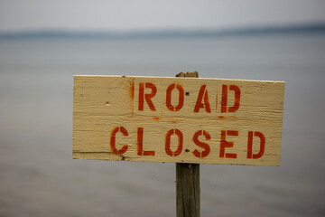 A sign that states the road is closed - bear wood and red letters made with stencils and spray paint