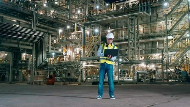 Male expert is using a laptop on the premises of the refinery plant
