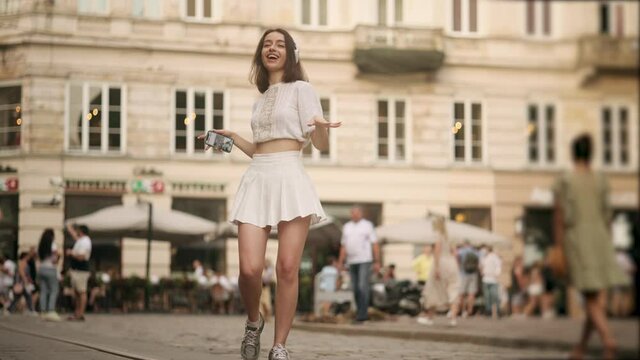 Happy cool woman wearing headphones dancing alone on street. Young adult happy girl dancing in downtown very emotional. Modern lifestyle and happiness concept